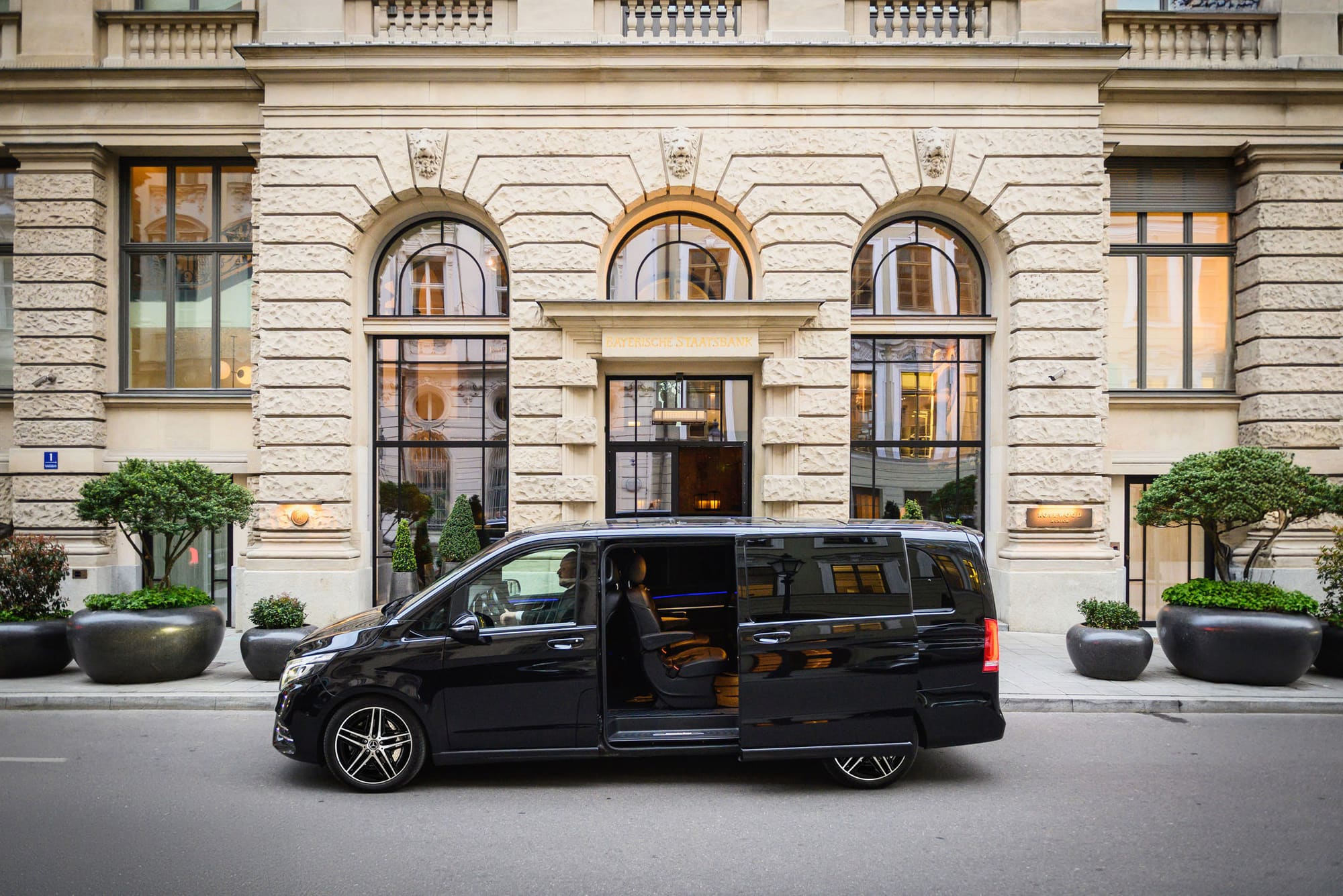 Black AYDEN Mercedes-Benz V-Class with its sliding door open outside the historic façade of the Bayerische Staatsbank in Munich