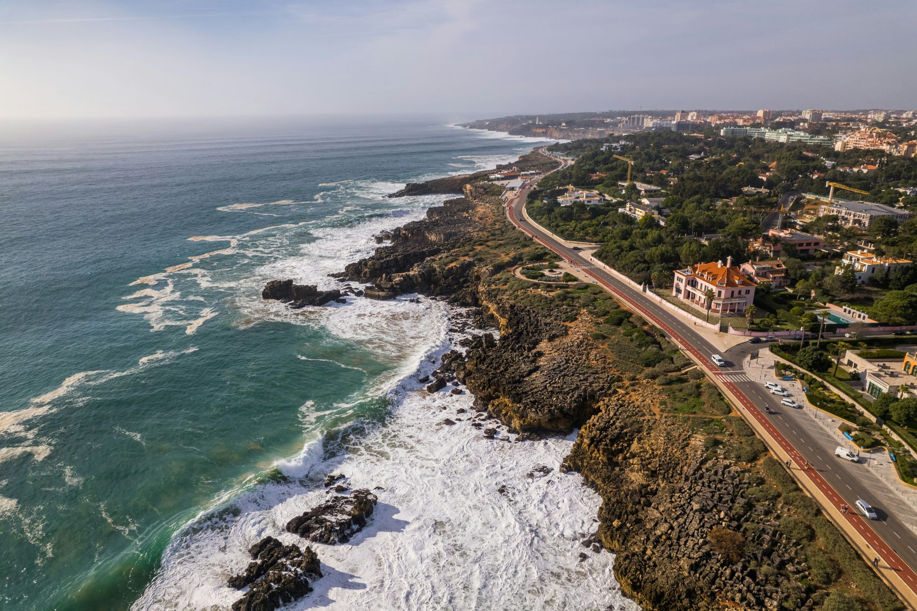 Aerial view of the rocky coast at Boca do Inferno in Cascais, with the coastal road Avenida Rei Humberto II de Itália, its cycle lane and villas alongside
