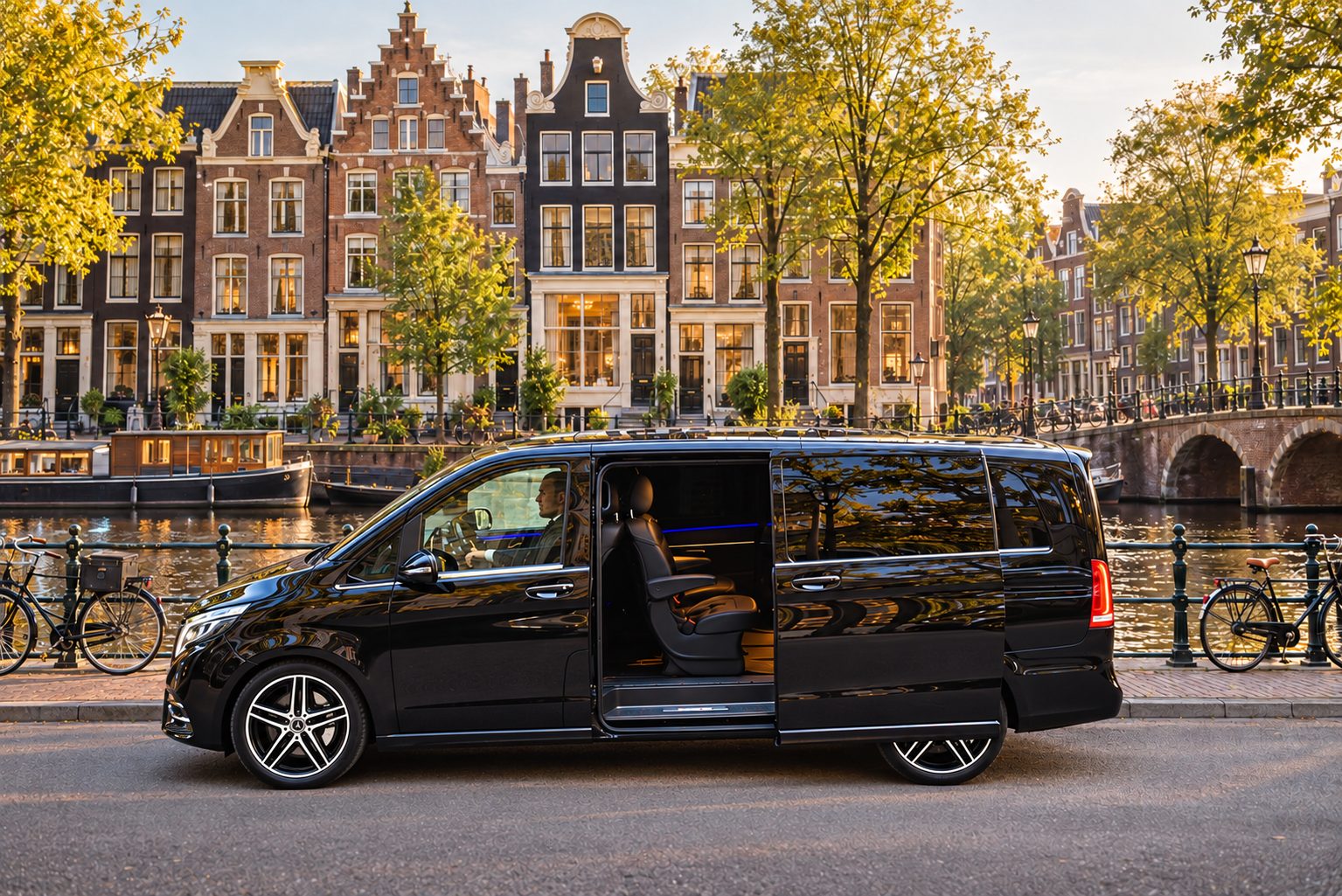 Chauffeurservice Amsterdam: schwarze Mercedes-Benz V-Klasse mit geöffneter Schiebetür an einer Gracht vor historischen Giebelhäusern