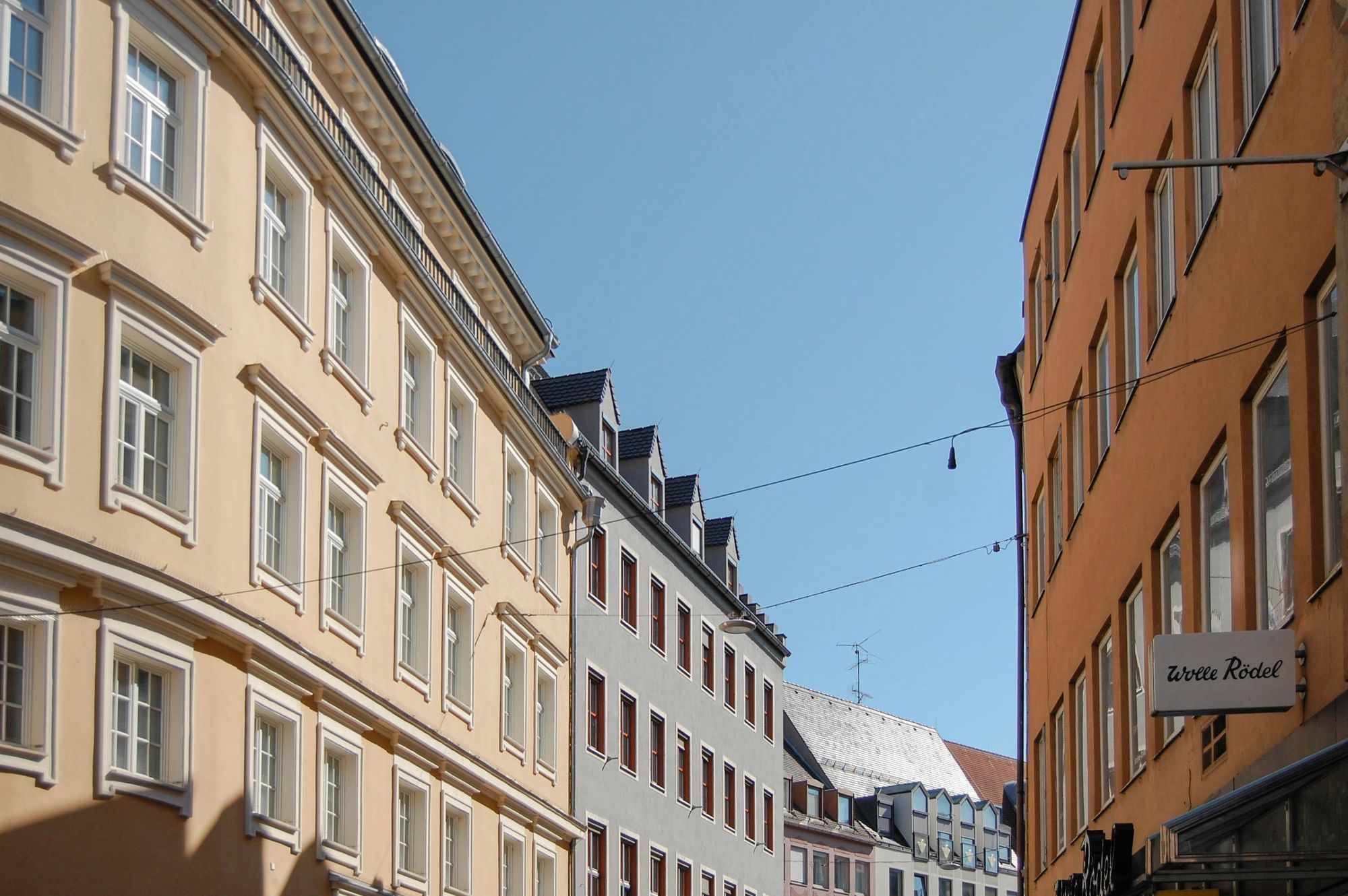 Altbaufassaden in Gelb, Grau und Orange an einer Straße in Augsburg unter blauem Himmel