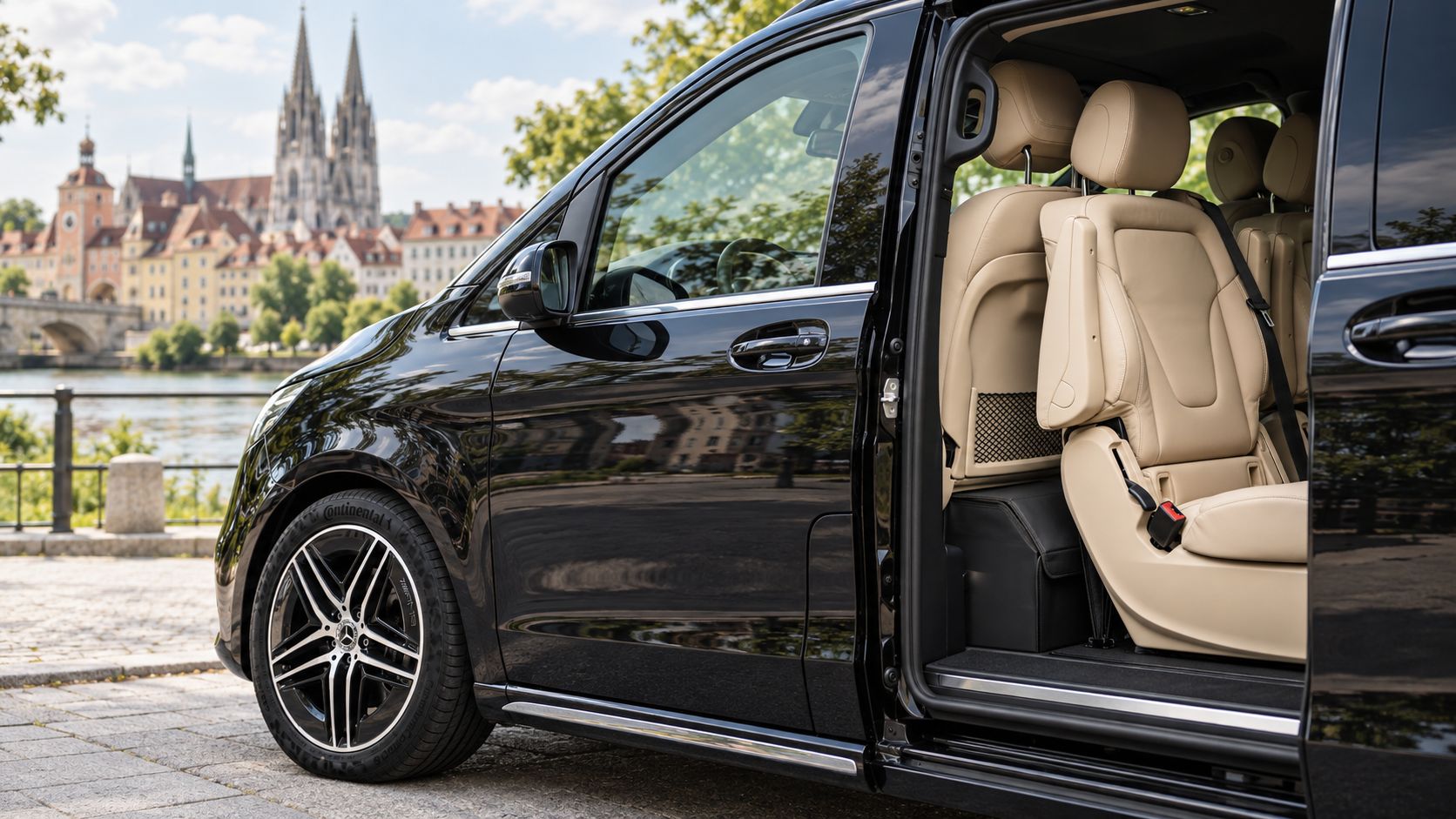 Flughafentransfer Regensburg: schwarze Mercedes-Benz V-Klasse mit geöffneter Schiebetür und hellen Ledersitzen, im Hintergrund Steinerne Brücke, Altstadt und Dom