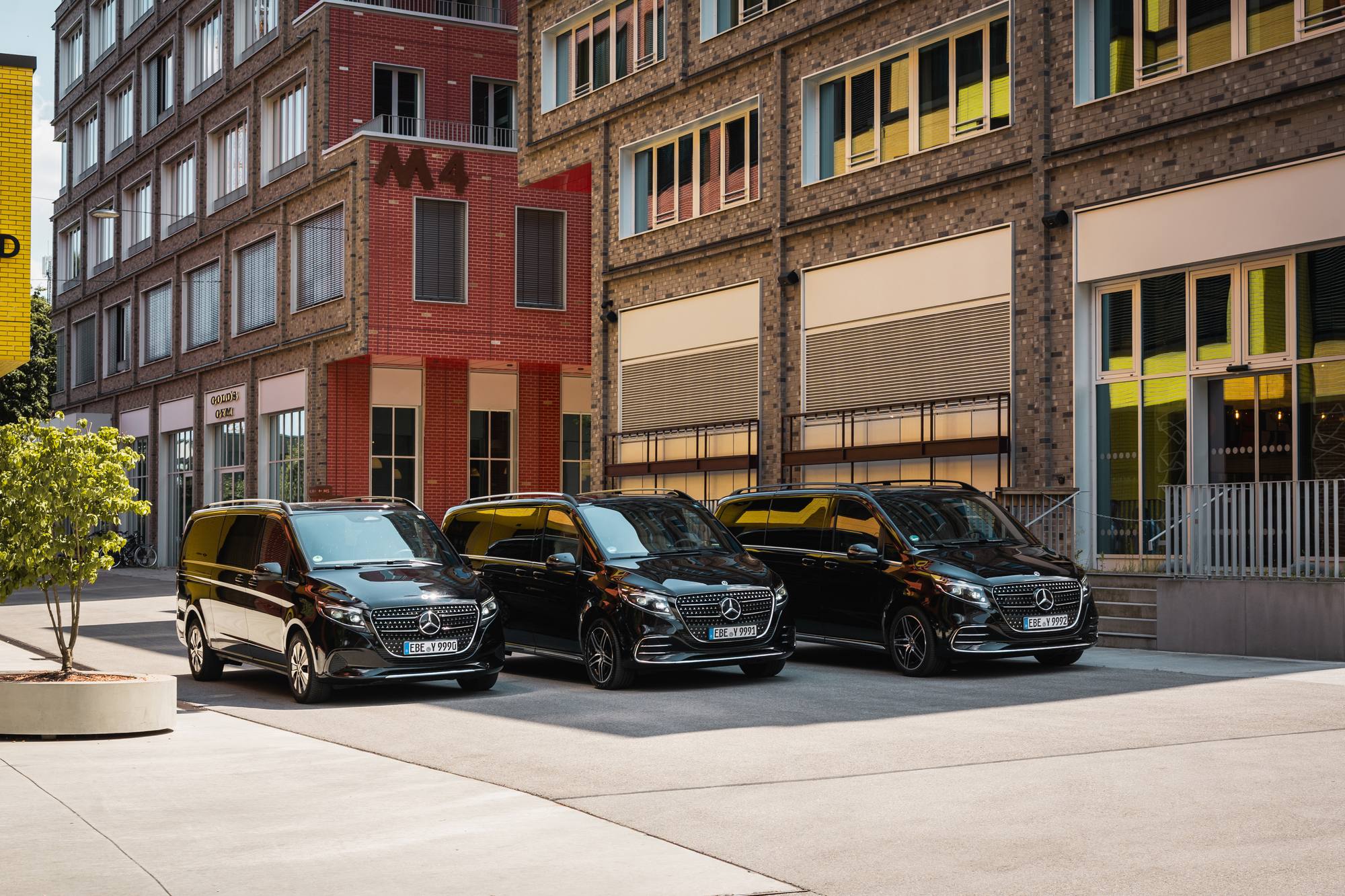 Three black AYDEN Mercedes-Benz V-Class vans side by side in front of brick buildings