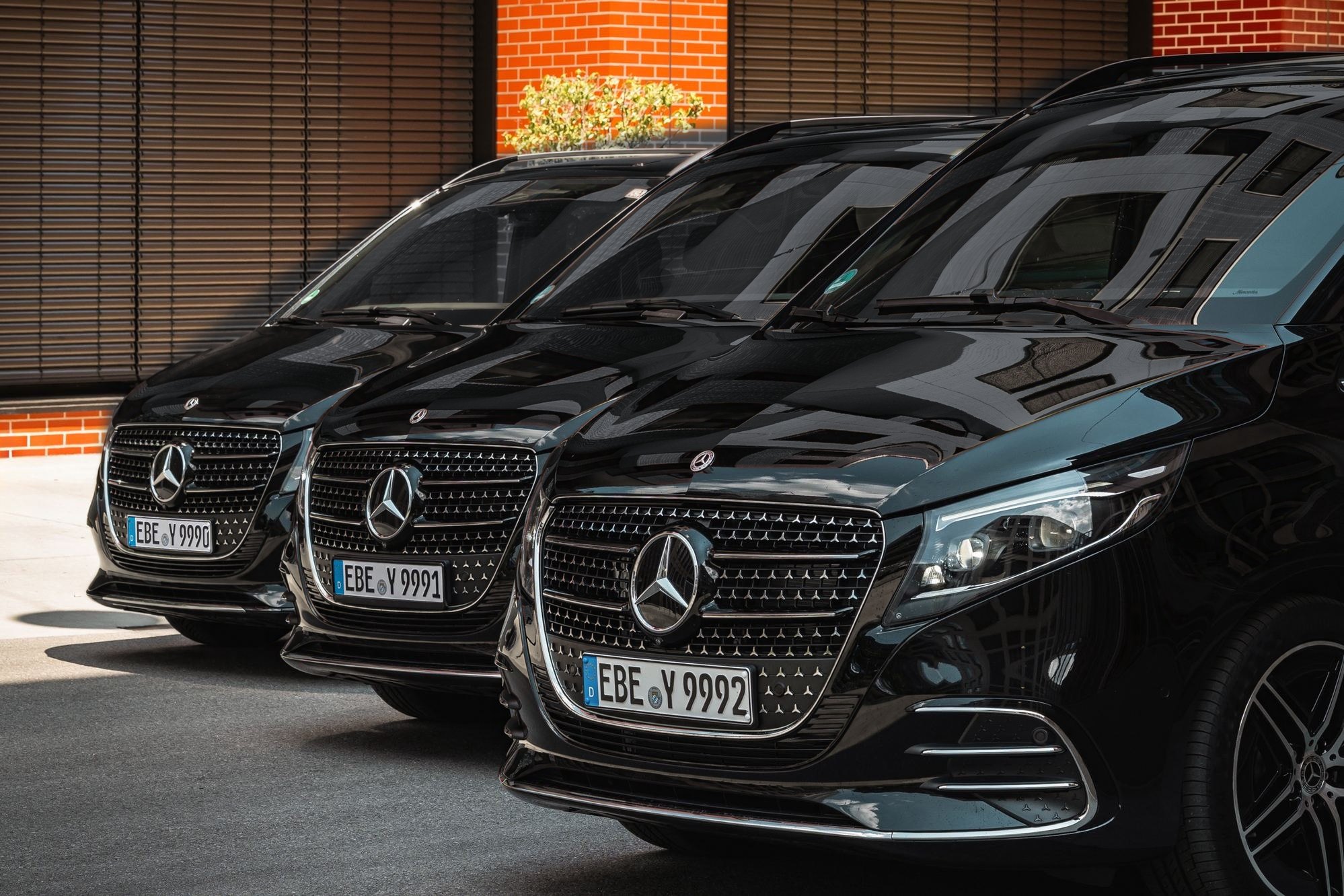 Drei schwarze Mercedes-Benz V-Klassen von AYDEN nebeneinander vor einer Backsteinfassade