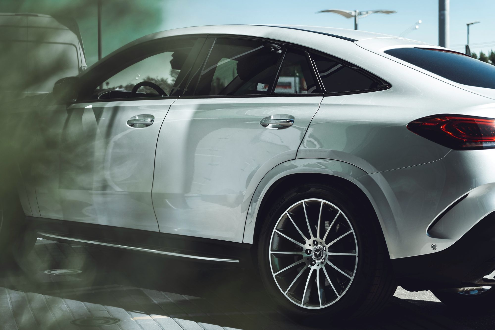 Silver Mercedes-Benz SUV coupé from the side, blurred leaves in the foreground