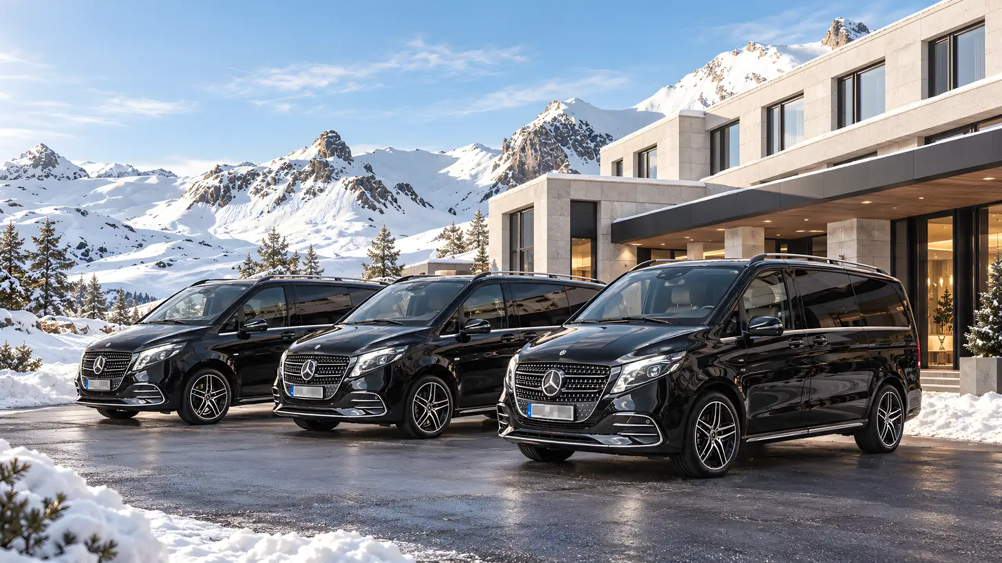 Drei schwarze Mercedes-Benz V-Klassen vor einem modernen Hotel, dahinter verschneite Berggipfel – Skitransfer von AYDEN