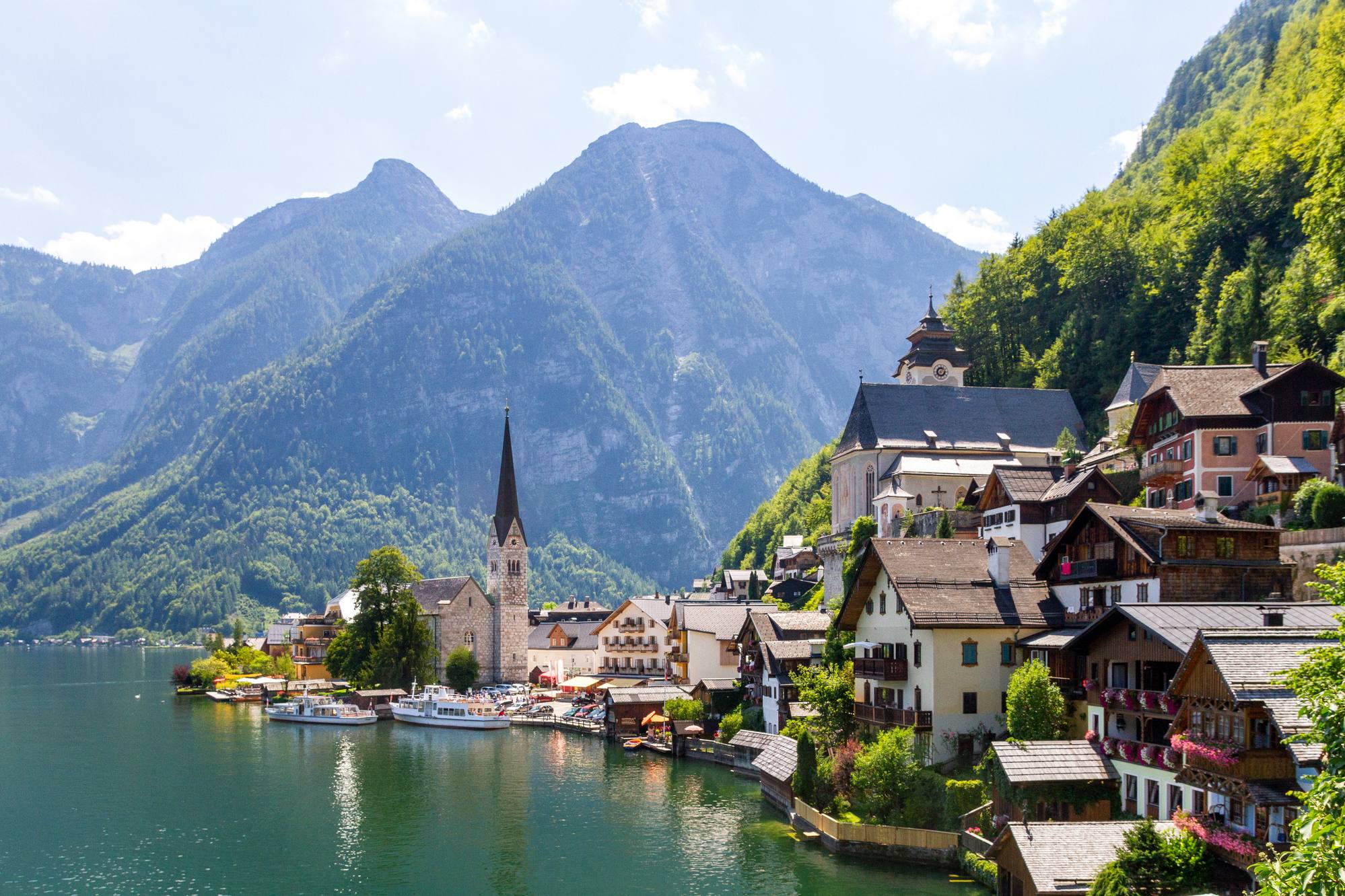 Hallstatt am Hallstätter See: Kirchturm und Häuser am Ufer vor bewaldeten Bergen im Sommer