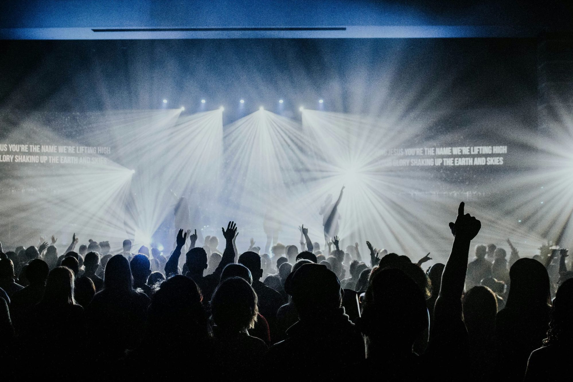 Audience with raised hands in front of a brightly lit concert stage